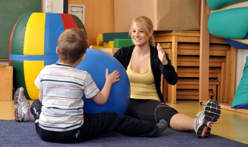 Junge blonde Physiotherapeuten, die Übungen mit einem kleinen Jungen macht. Kinder Physiotherapie.