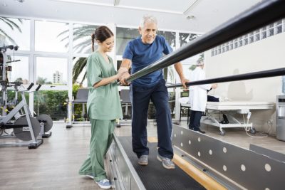 Junge Physiotherapeutin, die mit einem älteren Patienten in der Rehabilitation arbeitet.