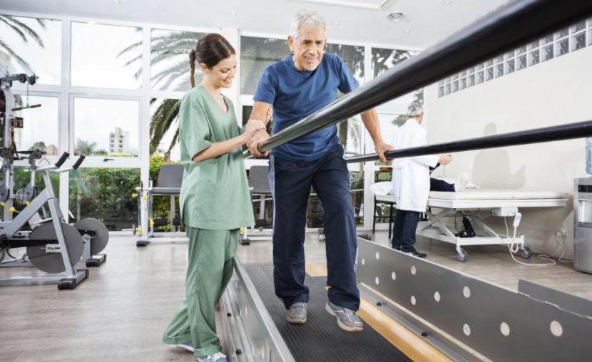 Junge Physiotherapeutin, die mit einem älteren Patienten in der Rehabilitation arbeitet.