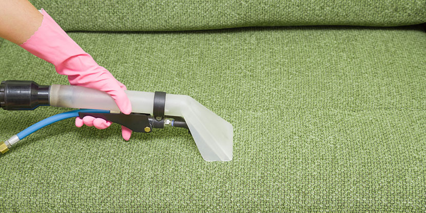 Sofa reinigen: Eine professionelle Reinigungskraft reinigt ein grünes Sofa mit einem Dampfreiniger.
