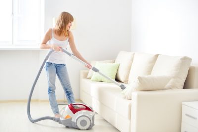 Junge blonde Frau beim Sofa reinigen mit dem Staubsauger.