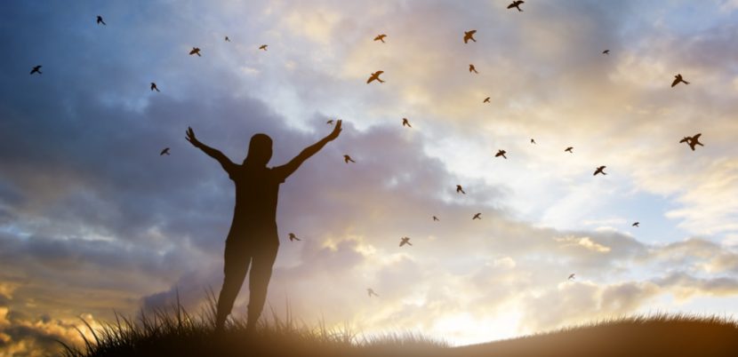 Junge Frau, die im Morgengrauen im Freien steht und eine Siegerpose einnimmt. Am Himmel fliegen Vögel. Familienaufstellung Wien, Graz, Linz.