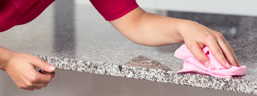 Granit reinigen: Eine Frau reinigt eine Granitplatte mit einem rosa Tuch