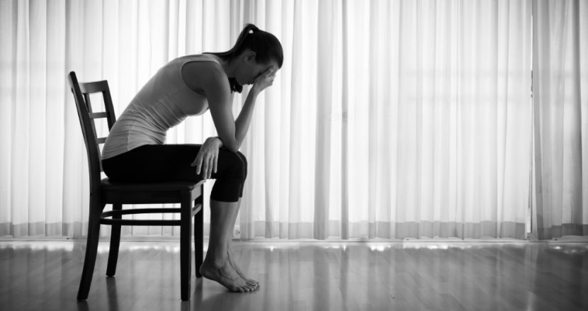 Junge Frau, die im abgedunkelten Raum auf einem Stuhl sitzt und den Kopf in die Hände stützt. High Functioning Depression.