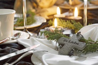 Festliches Gedeck an der Leichenschmaus Tafel mit brennenden Kerzen und einem Holzkreuz. Leichenschmaus Lokale Wien.