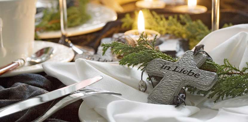 Festliches Gedeck an der Leichenschmaus Tafel mit brennenden Kerzen und einem Holzkreuz. Leichenschmaus Lokale Wien.