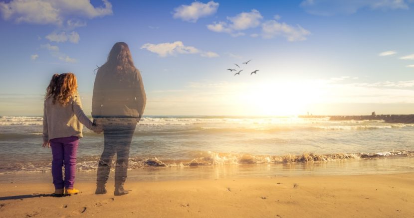 Mädchen am Strand bei Sonnenuntergang, hält die Hand ihrer verstorbenen Mutter, die ihr als Geist erscheint. Trauer Therapie Wien.
