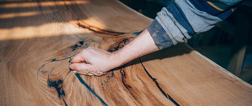 Mit Epoxidharz Holz versiegeln: Ein Mann streicht mit der Hand über einen polierten Epoxid Laminierharz Tisch.