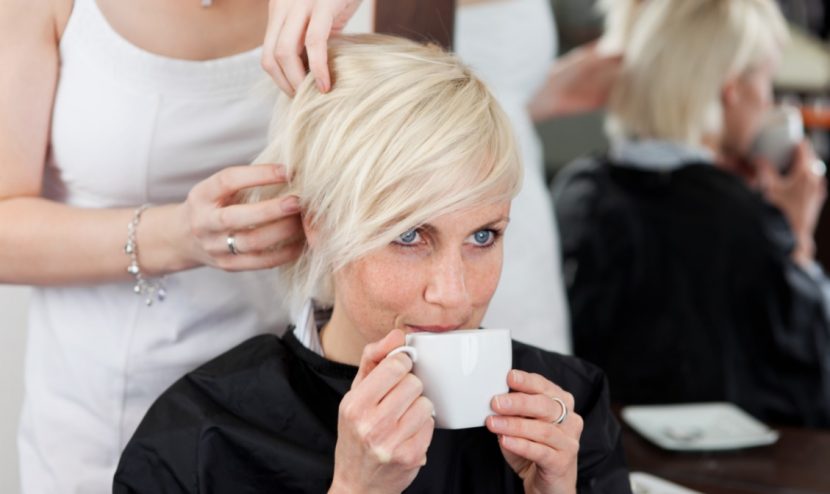 Junge blonde Frau, die beim Friseur Graz entspannt einen Kaffee trinkt, während sie eine neue Frisur bekommt.