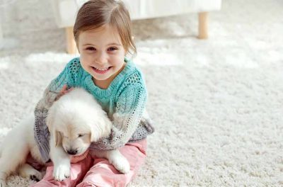 Teppichboden verlegen: Ein kleines Mädchen spielt mit einem Welpen auf einem Teppichboden.