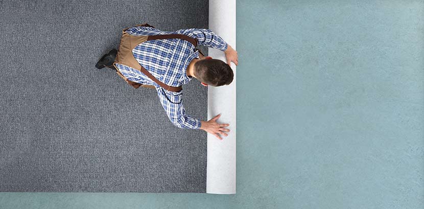Teppich verlegen: Ein Mann rollt einen Teppichboden aus.