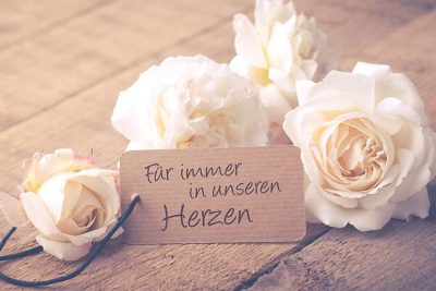 Vier weiße Rosen verteilt um einen Schild, das sich auf einen Todesfall bezieht. Todesfall Checkliste Österreich.