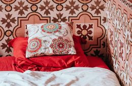 Fliesen auf Fliesen kleben: Ein Bett mit rot-weißem Bezug steht vor einer Wand mit marokkanischen Fliesen in Rot-Tönen.
