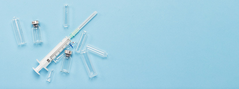 Eine Spritze und verschiedene Kanülen, mit der die Masern Impfung durchgeführt wird, auf einem blauen Untergrund.