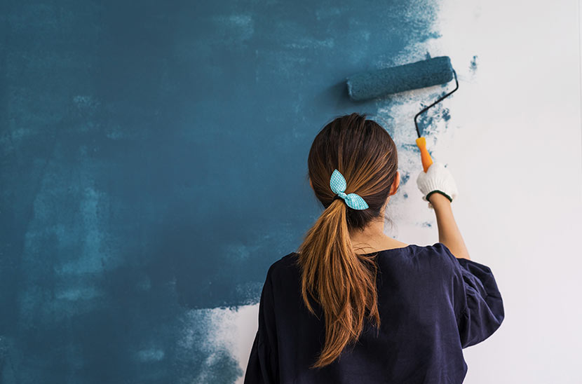 Wohnung streichen: Eine junge Frau streicht eine Wand mit blauer Farbe.