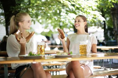 Biergärten Wien: Zwei junge Frauen sitzen im Biergarten, trinken Bier und essen Brezln.