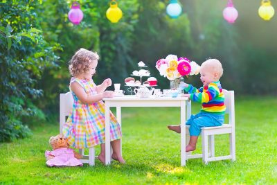 Gartenmöbel Kinder: Zwei Geschwister sitzen draußen auf Gartensesseln und spielen zusammen ein Garten Spiel.