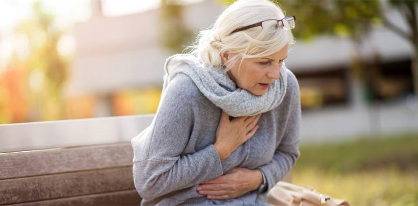Frau in mittlerem Alter, die auf einer Bank sitzt und plötzlich Atemnot und Brustschmerzen bekommt. Kardiologe Wien.