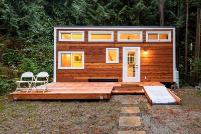 Ein Tiny House aus Holz steht im Wald.