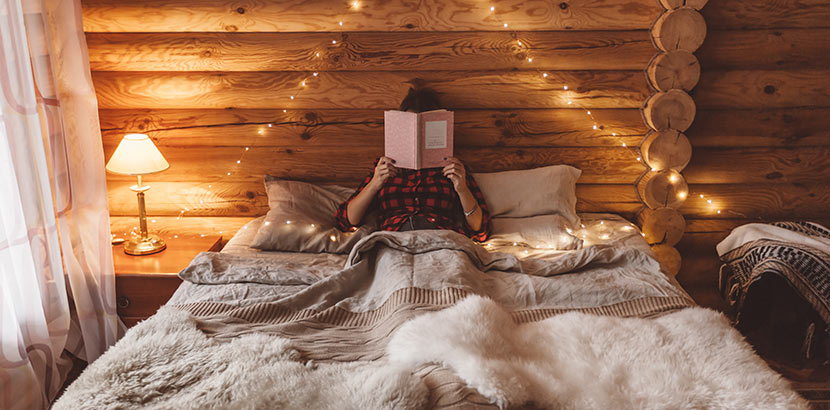 Eine Frau sitzt in ihrem Tiny House aus Holz und liest entspannt ein Buch. Im Minihaus lässt es sich perfekt abschalten.