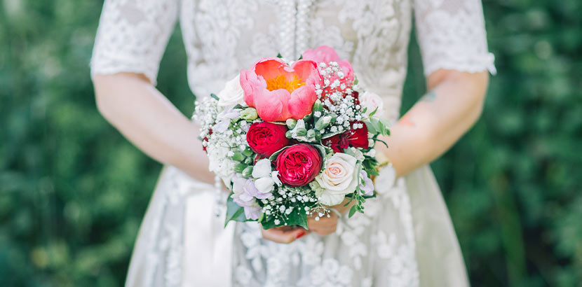 Eine Frau hält einen Brautstrauß mit Rosen, Schleierkraut und einer Pfingstrose.