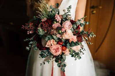 Eine Braut hält einen romantischen, modernen Brautstrauß mit roten Blumen