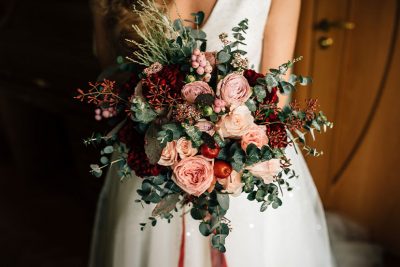 Eine Braut hält einen romantischen, modernen Brautstrauß mit roten Blumen