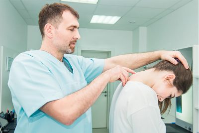 Neurologe Wien, der eine Patientin untersucht und ihr dafür die Wirbelsäule im Nackenbereich abtastet.