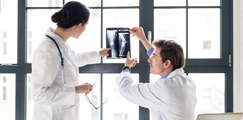 Ein Orthopäde und eine Orthopädin, die über eine Röntgenaufnahme diskutieren.