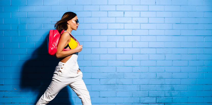 Junge Hipster-Frau mit pinkem Turnbeutel vor einer blauen Wand.