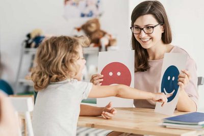Junge dunkelhaarige Kinderpsychologin, die mit einem kleinen Mädchen arbeitet.