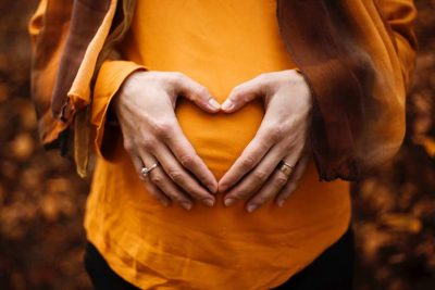 Mutter-Kind-Pass: Eine schwagere Frau hält sich die Hände über ihrem Schwangerschaftsbauch.