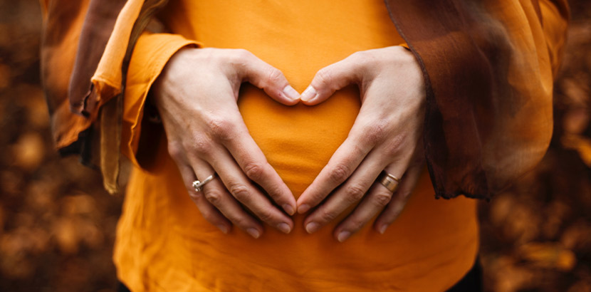 Mutter-Kind-Pass: Eine schwagere Frau hält sich die Hände über ihrem Schwangerschaftsbauch.