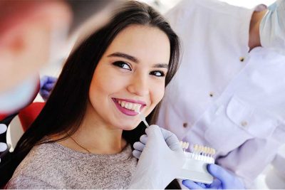 Junge hübsche dunkelhaarige Patientin beim Zahnarzt, die sich Veneers anpassen und einsetzen lässt.