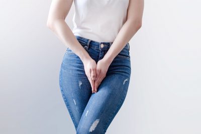Unterkörper einer jungen Frau, die die Hände vor dem Schritt verschränkt. Inkontinenz, Harninkontinenz.