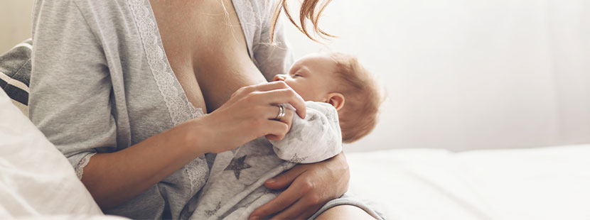 Junge Frau mit großen Brüsten, die ihren Säugling stillt. Brustverkleinerung Kosten Wien.