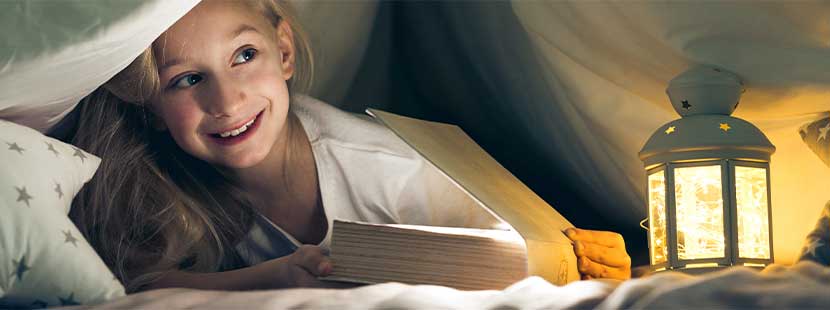 Blondes Mädchen, das nachts unter der Decke ein Buch liest. Kinderbuchhandlung Wien.