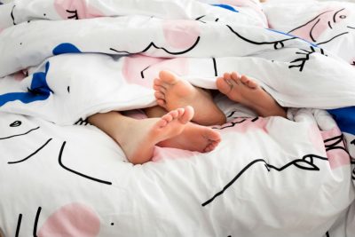 Geschlechtskrankheiten: Vier Füße schauen unter einer Bettdecke hervor.