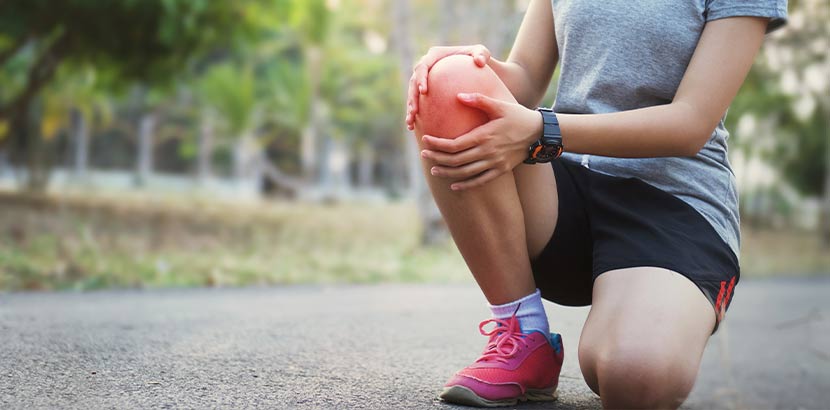 Junge Joggerin mit Knieproblemen, die auf der Straße kniet und sich das Knie hält. Sportmediziner Wien.