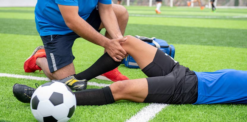 Fußballer, der auf dem Spielfeld von einem Sportmediziner behandelt wird. Sportarzt Wien.