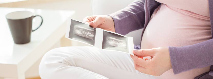 Schwangere, die nach einer efolgreichen künstlichen Befruchtung zwei Ultraschallbilder ihres ungeborenen Kindes in der Hand hält.