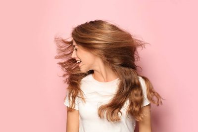 Junge Frau mit starkem, schönem Haar nach der PRP Haare Behandlung vor rosafarbenem Hintergrund.