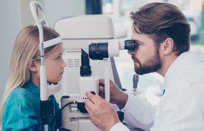 Ein Augenarzt untersucht mithilfe einer Spaltlampe die Augen eines Kindes. Augenarzt Graz.