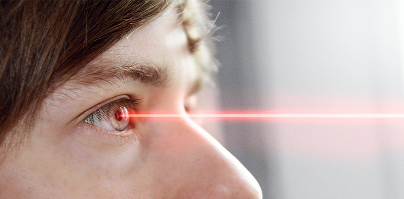 Eine Nahaufnahme von dem Auge einer Frau, auf das ein roter Laserstrahl trifft. Augenarzt Linz.