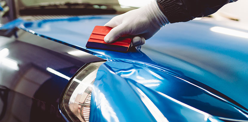 Eine blaue Autofolie auf einer Motorhaube wird mit einem Werkzeug geglättet.