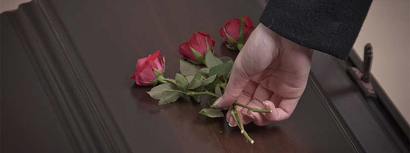 Frauenhand, die bei einer Bestattung rote Rosen auf einen dunklen Sarg legt. Bestatter Wien.