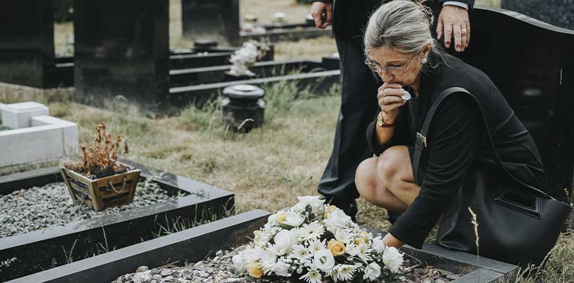 Ältere Frau mit grauen Haaren und Trauerkleidung, die an einem frischen Grab trauert. Bestatter Wien.
