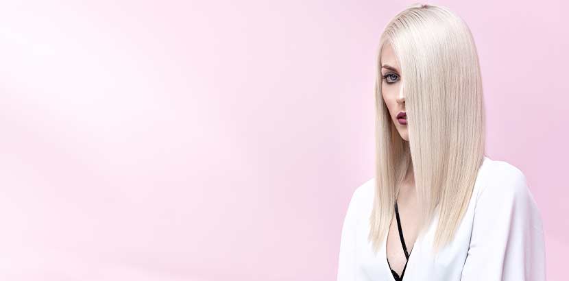 Junge Frau mit weißblond gefärbten langen Haaren vor rosa Hintergrund. Friseur Linz.
