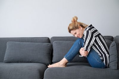 Junge blonde Frau, die sich vor Magenschmerzen auf einem Sofa windet. Gastroenterologe Wien.