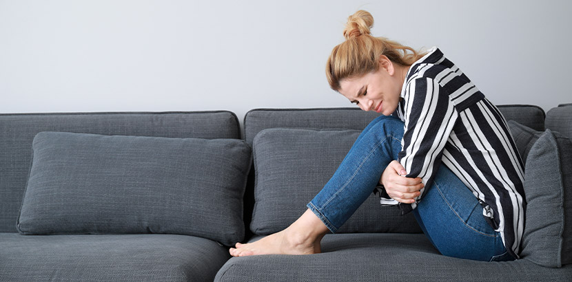 Junge blonde Frau, die sich vor Magenschmerzen auf einem Sofa windet. Gastroenterologe Wien.